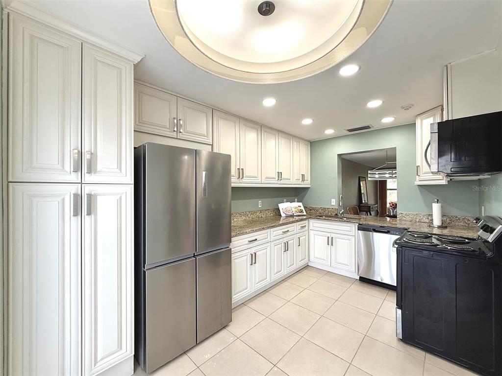 A kitchen features white cabinetry, stainless steel appliances, granite countertops, and light-colored tile flooring — 942 N BENEVA ROAD UNIT V28, SARASOTA, FL