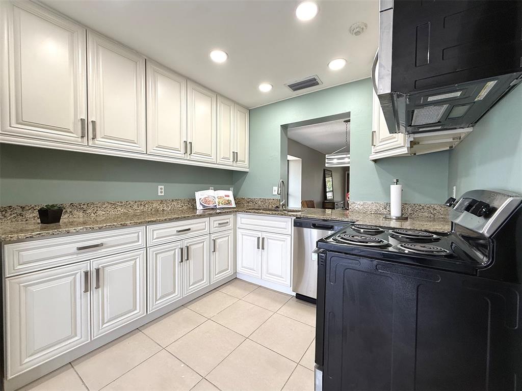 A kitchen features white cabinets, granite countertops, a black stove, and light green walls — 942 N BENEVA ROAD UNIT V28, SARASOTA, FL
