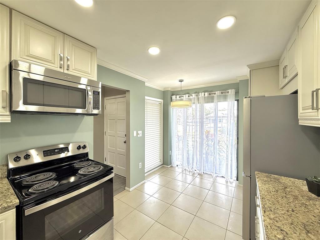 A kitchen features light-colored cabinets, stainless steel appliances, granite countertops, and a tiled floor — 942 N BENEVA ROAD UNIT V28, SARASOTA, FL