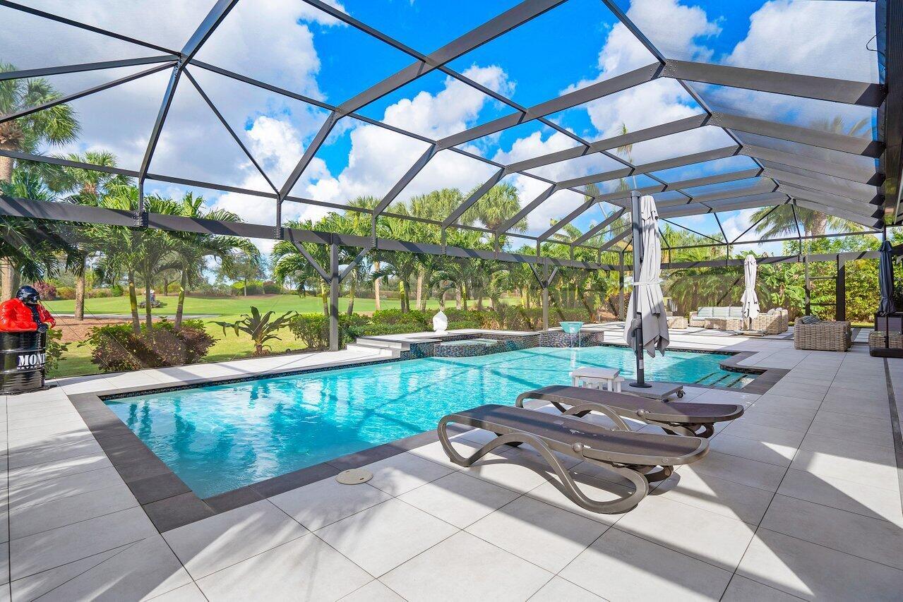 A swimming pool with a spa sits inside a screened-in lanai overlooking a grassy lawn — 4848 Chamal Circle, Boca Raton FL 33487, BOCA RATON, FL