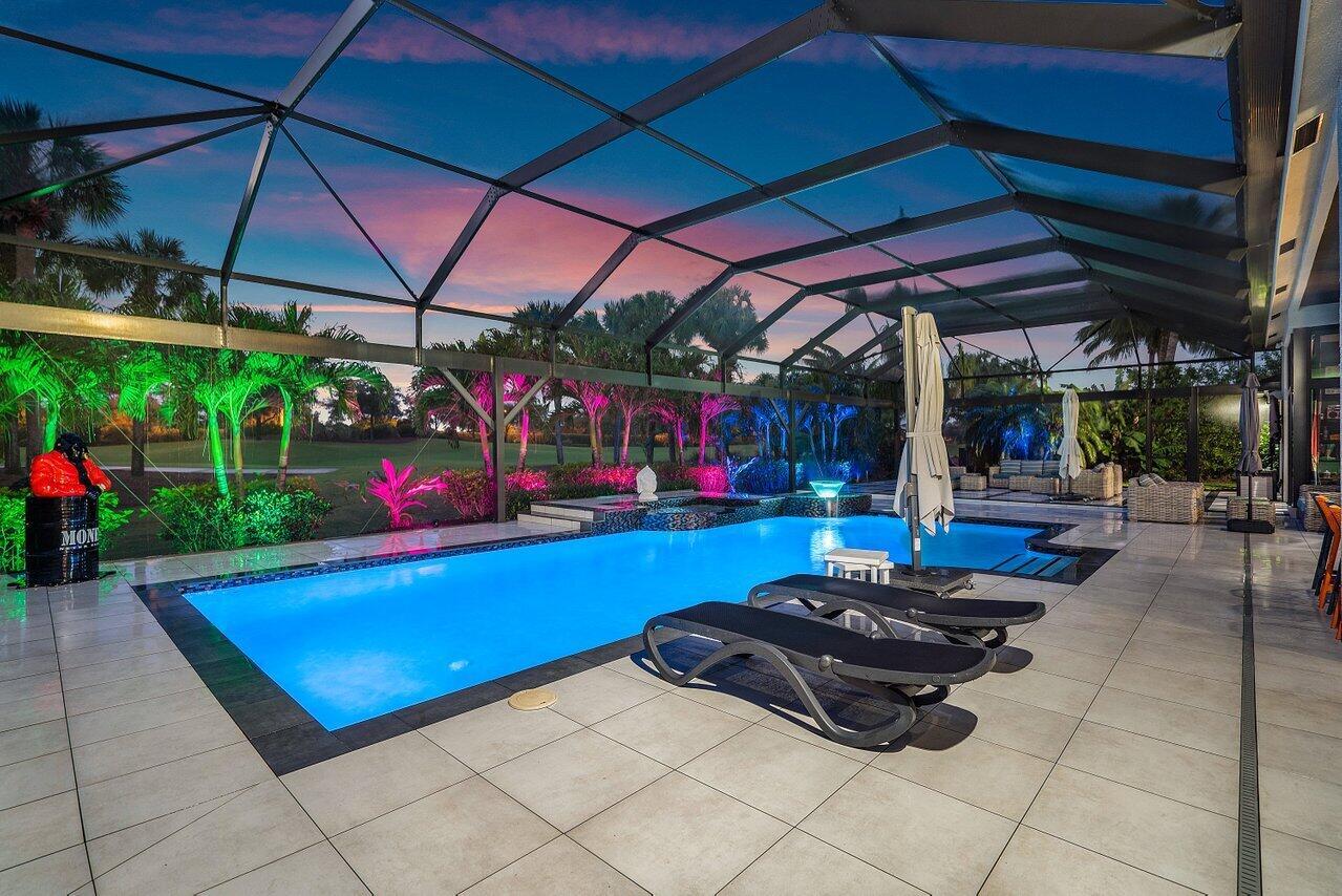 A swimming pool with lounge chairs sits inside a screened-in patio at sunset — 4848 Chamal Circle, Boca Raton FL 33487, BOCA RATON, FL