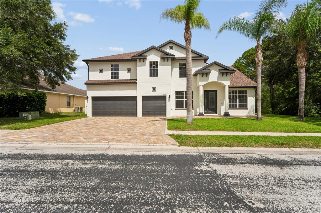A two-story house with a paved driveway, three-car garage, and two palm trees in front — 14229 LEYBOURNE WAY, SPRING HILL, FL