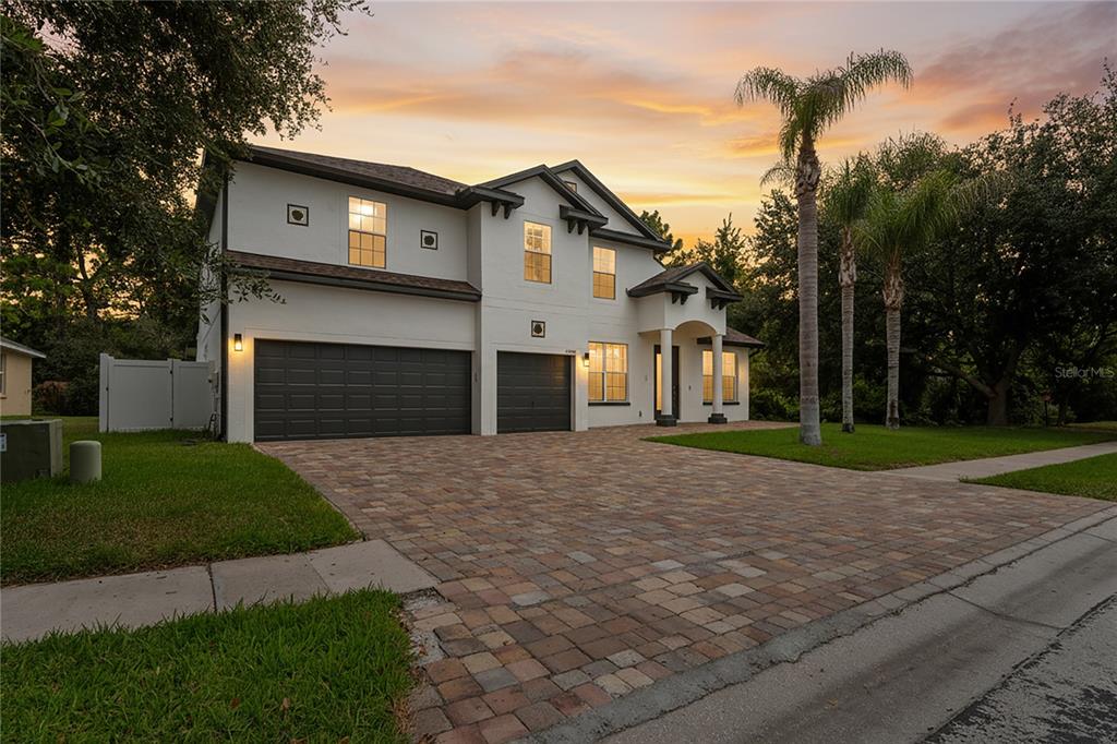 A two-story house with a paver driveway, three-car garage, and white stucco exterior at sunset — 14229 LEYBOURNE WAY, SPRING HILL, FL