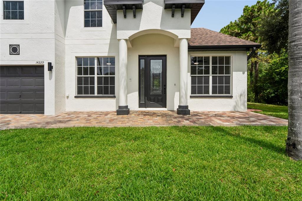 A two-story house exterior features a paved walkway, a dark front door, and a garage — 14229 LEYBOURNE WAY, SPRING HILL, FL