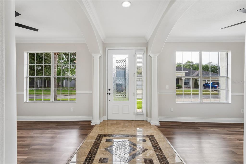 A foyer with a tiled inlay floor, white columns, and a glass-paneled front door — 14229 LEYBOURNE WAY, SPRING HILL, FL