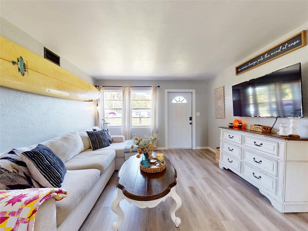 A living room features a surfboard on the wall, a sectional sofa, and a television — 903 CONRAD DRIVE, NEW SMYRNA BEACH, FL