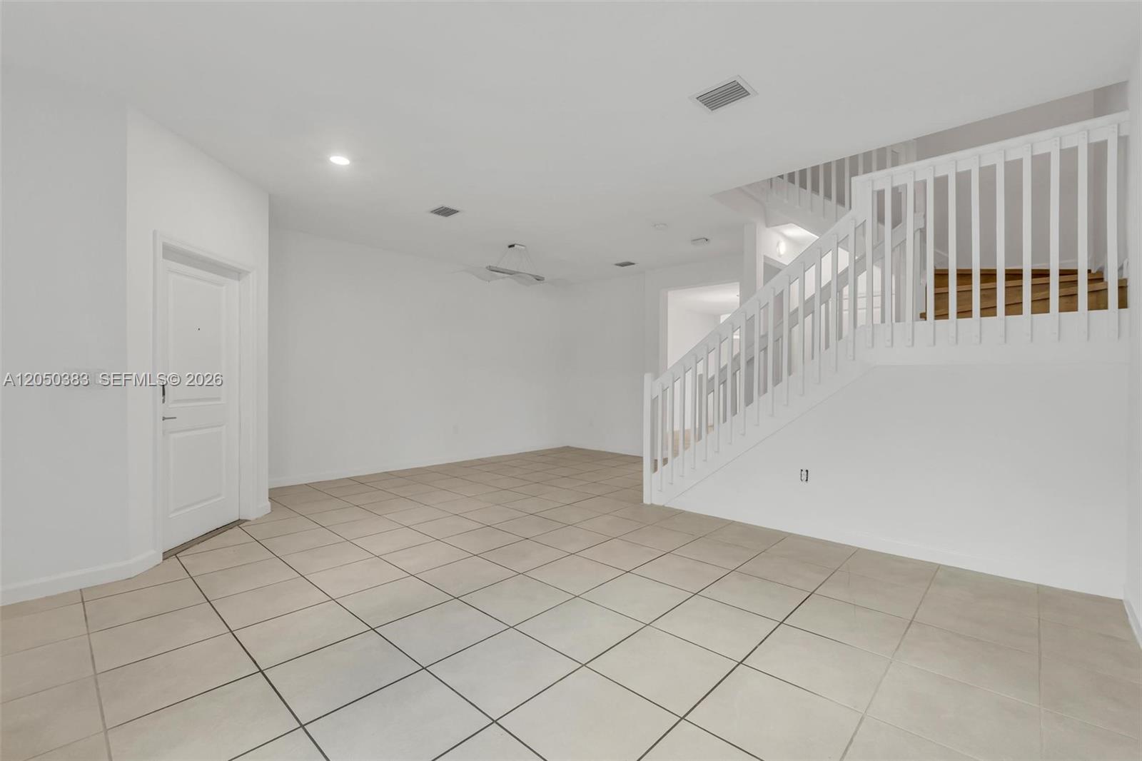 An empty room with white walls, tiled floors, and a white staircase with railings — 582 NE 207th St, Miami FL 33179, MIAMI, FL