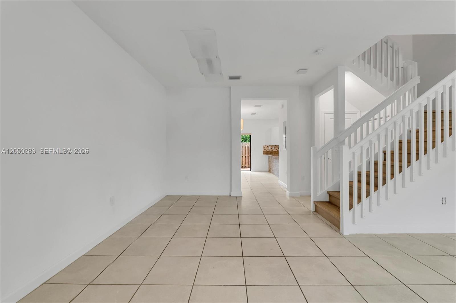 An empty room with light tile flooring features a white staircase and a doorway — 582 NE 207th St, Miami FL 33179, MIAMI, FL