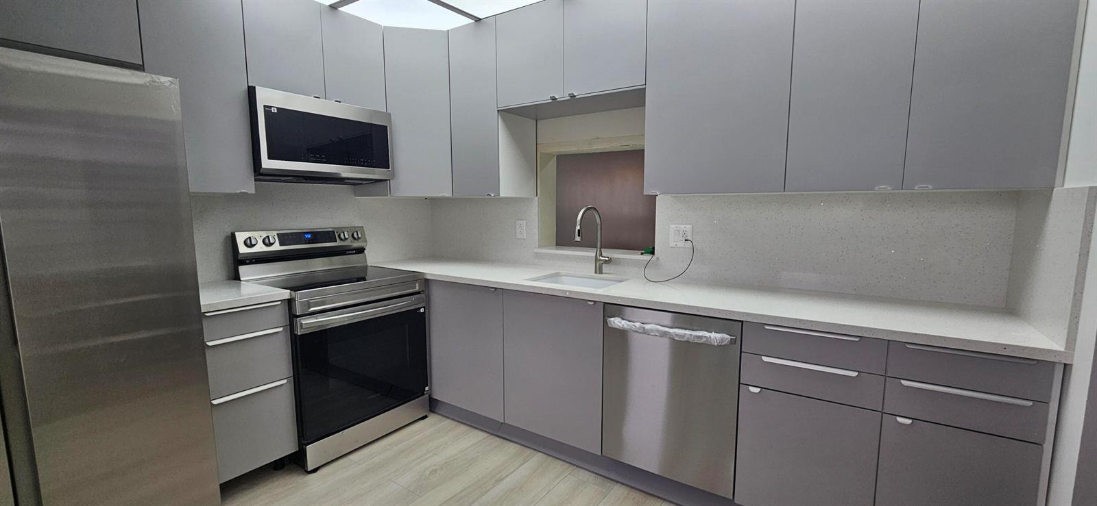 A modern kitchen features gray flat-panel cabinets, stainless steel appliances, and white quartz countertops — 421 NE 14th Avenue # 302, Hallandale Beach FL 33009, HALLANDALE BEACH, FL