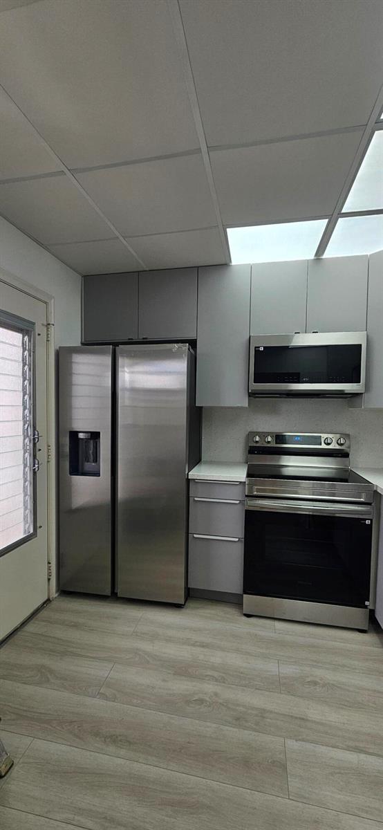 A kitchen features stainless steel appliances, gray cabinets, white countertops, and light wood-look flooring — 421 NE 14th Avenue # 302, Hallandale Beach FL 33009, HALLANDALE BEACH, FL