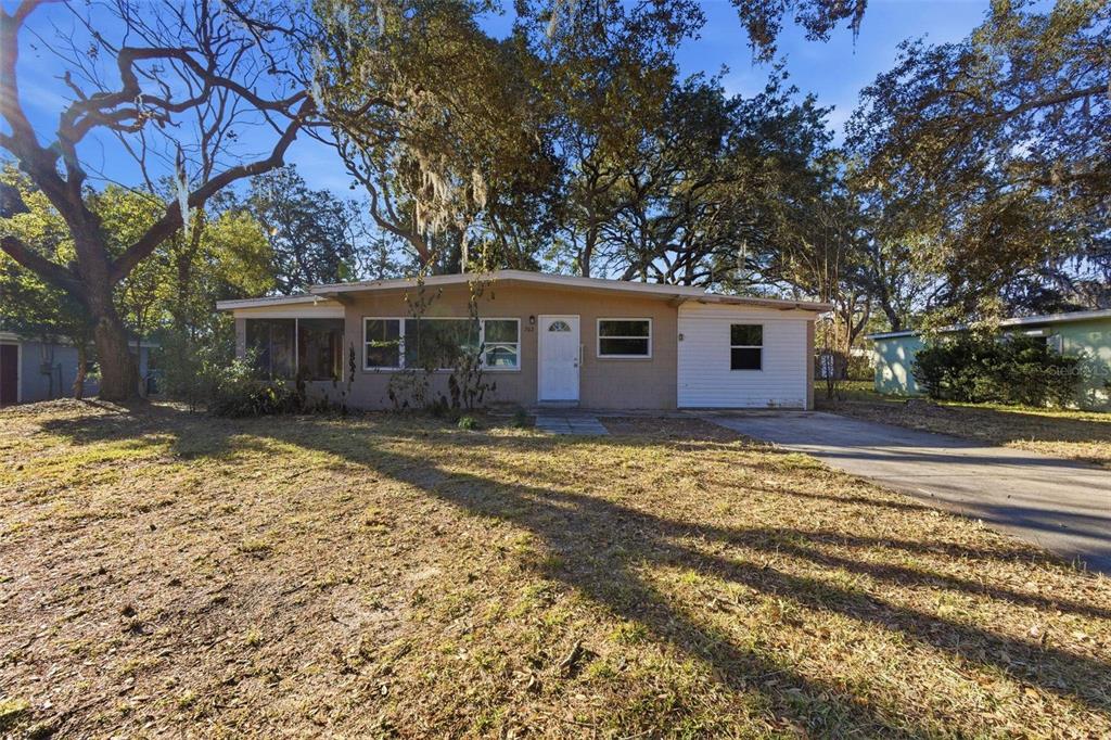A single-story house with a tan facade, white door, and a driveway under large trees — 762 VALENCIA AVENUE, ORANGE CITY, FL