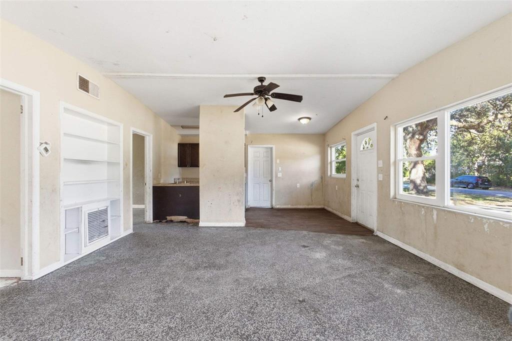A living room with gray carpet, built-in shelving, a ceiling fan, and a kitchen area — 762 VALENCIA AVENUE, ORANGE CITY, FL