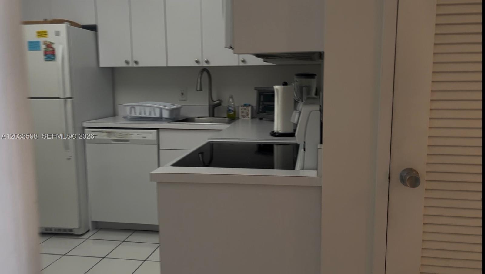 A kitchen features white cabinets, a white dishwasher, a refrigerator, and a black stovetop — 5161 Collins Ave # 1702, Miami Beach FL 33140, MIAMI BEACH, FL
