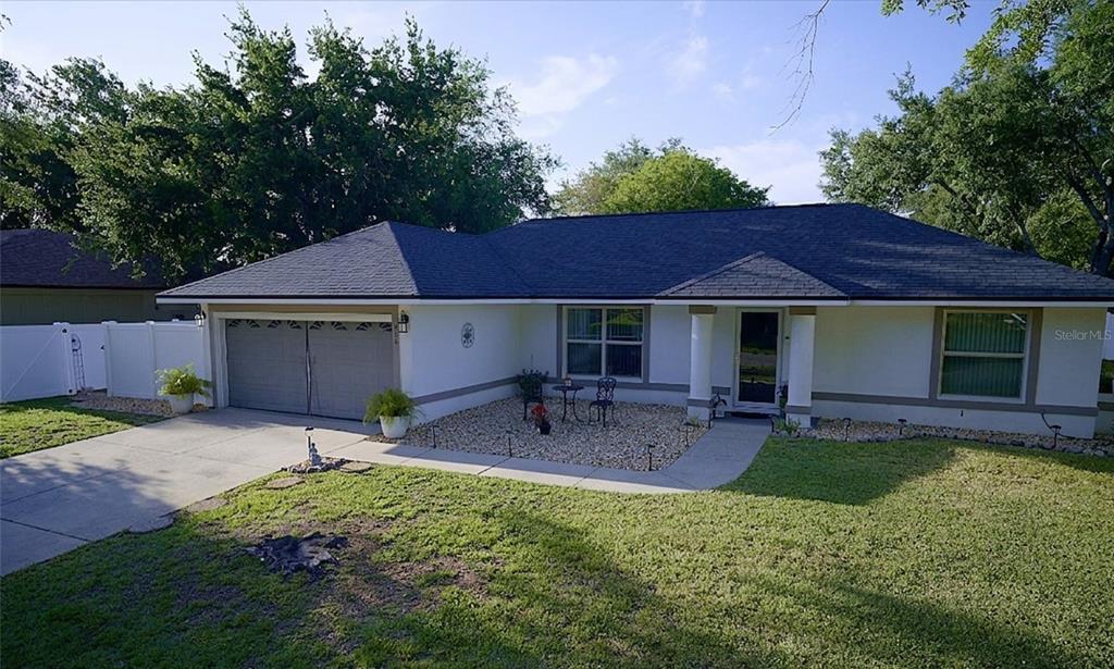 A single-story house with a white exterior, dark roof, two-car garage, and a gravel courtyard — 408 RAYMOND STREET, MINNEOLA, FL