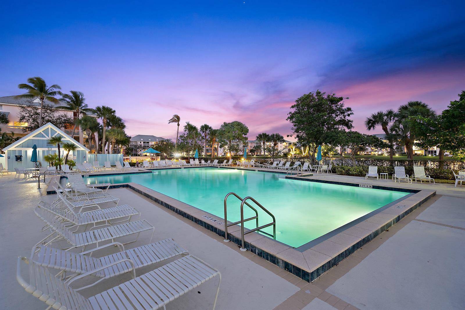 A swimming pool surrounded by lounge chairs at dusk with palm trees and buildings nearby — 353 S US Hwy 1 # f208, Jupiter FL 33477, JUPITER, FL