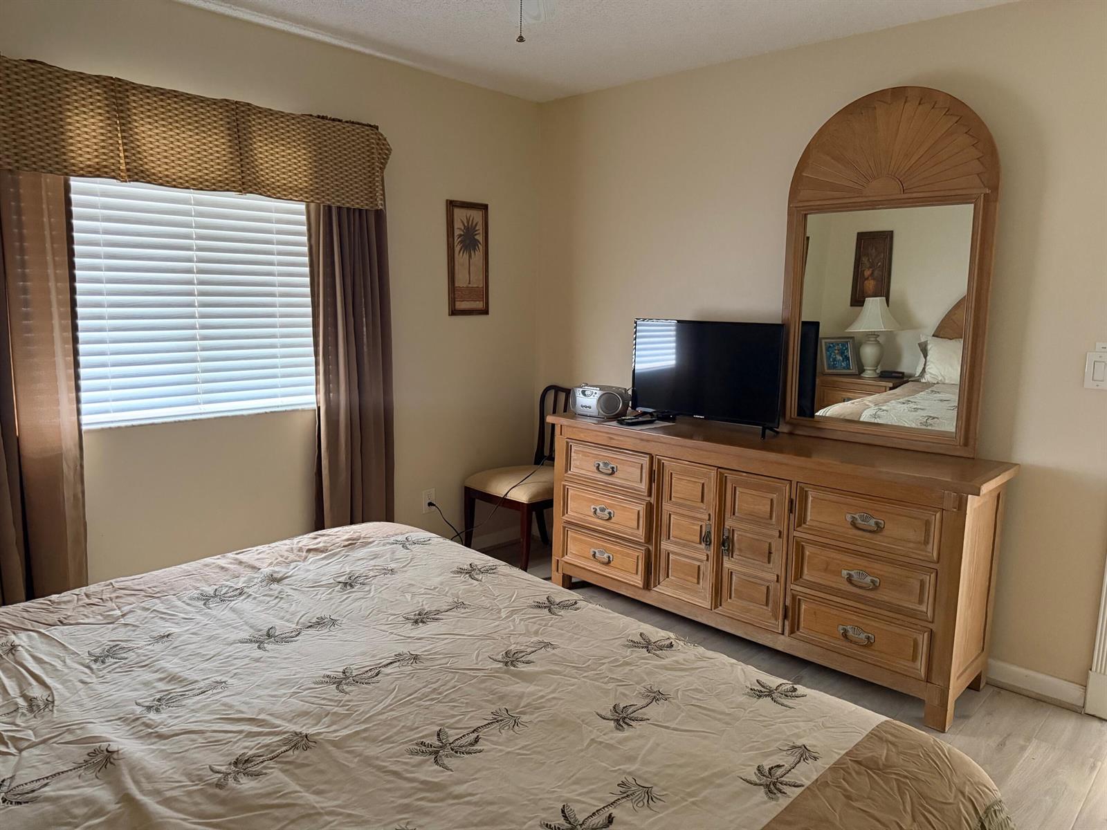 A bedroom features a bed with palm tree bedding, a wooden dresser, and a mirror — 353 S US Hwy 1 # f208, Jupiter FL 33477, JUPITER, FL