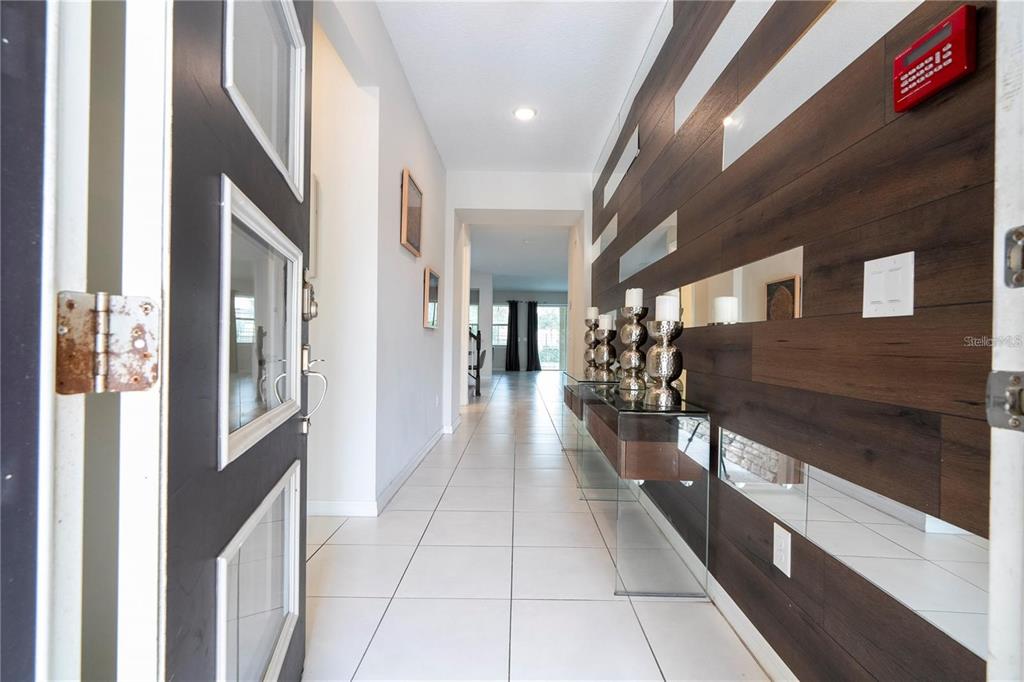 A bright entryway features white tile floors, a dark wood accent wall, and a glass console — 9043 SUNSHINE RIDGE LOOP, KISSIMMEE, FL