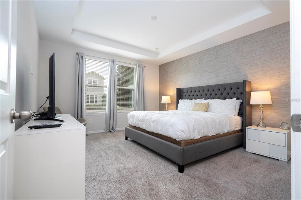 A bedroom features a gray tufted bed, white nightstands, and a textured accent wall — 9043 SUNSHINE RIDGE LOOP, KISSIMMEE, FL