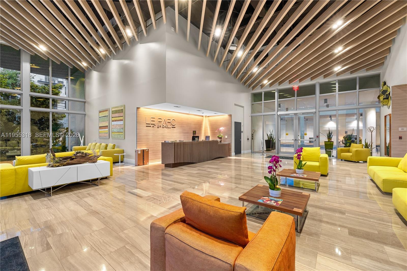 A modern building lobby features a reception desk, yellow seating, and a slatted wood ceiling — 1600 SW 1st Ave # 307, Miami FL 33129, MIAMI, FL