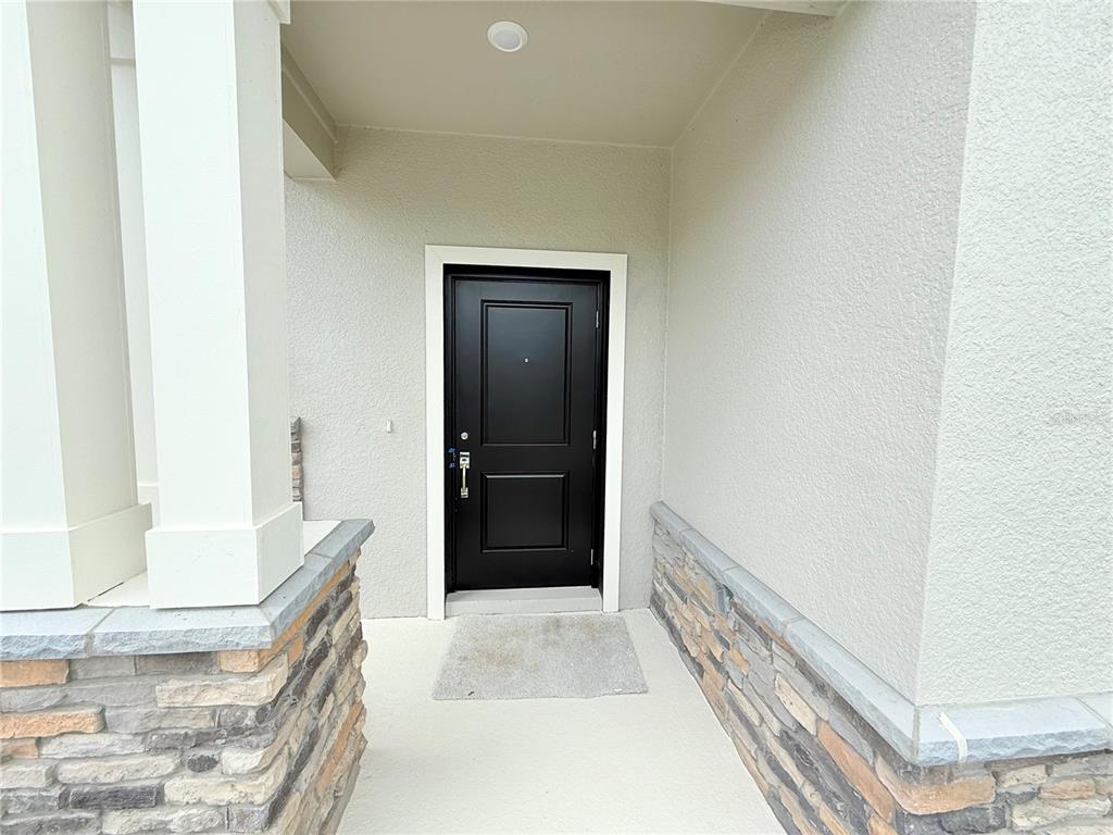A black front door is set within a covered porch featuring stone veneer accents — 623 TERRAPIN DRIVE, DEBARY, FL