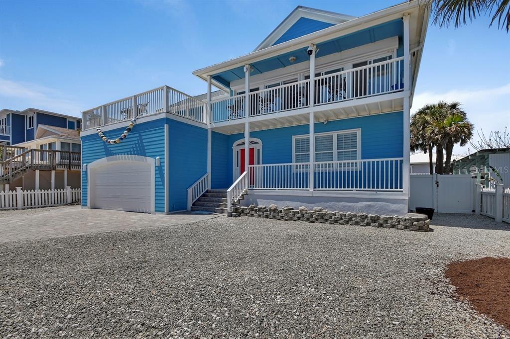 A bright blue two-story house features a white garage, wrap-around balconies, and a gravel driveway — 6344 S ATLANTIC AVENUE, NEW SMYRNA BEACH, FL