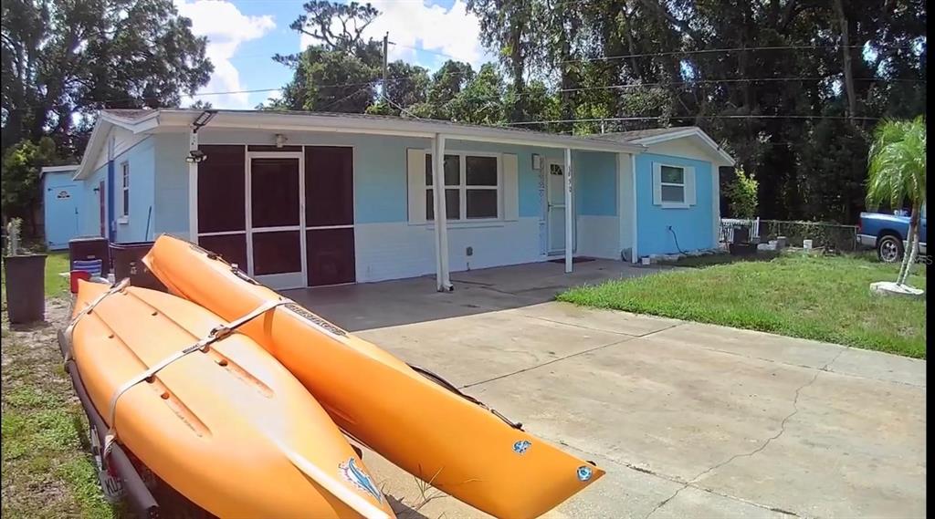 A light blue single-story house with a concrete driveway and two orange kayaks in front — 1650 BOLD LANE, HOLIDAY, FL