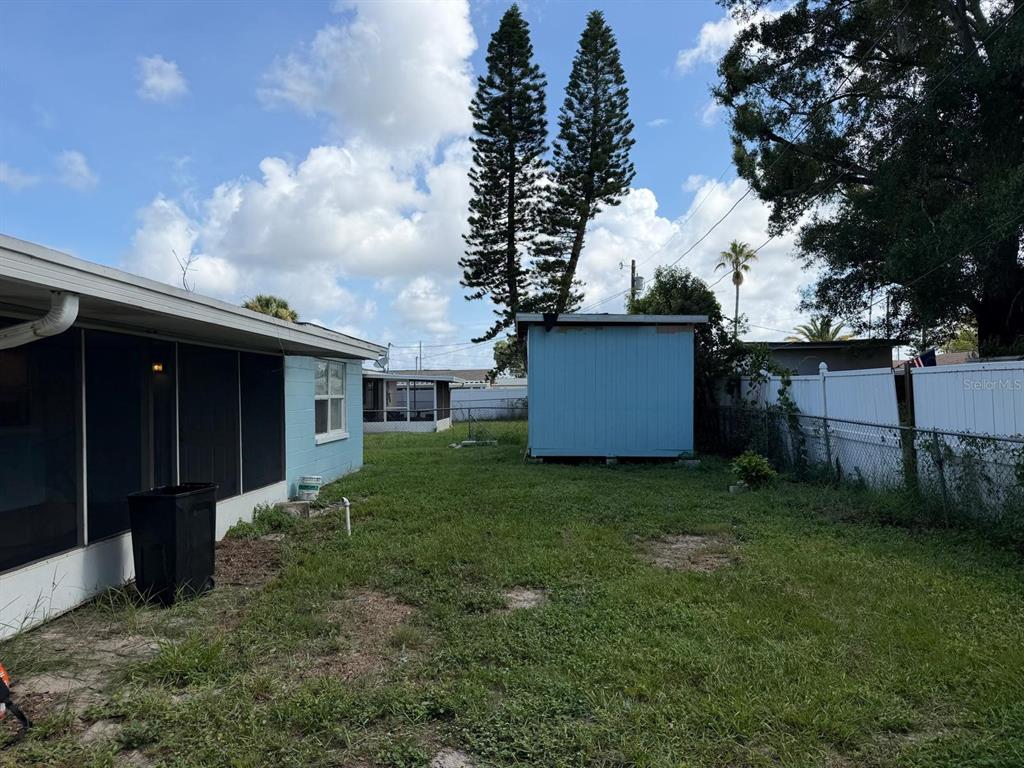 A backyard features a blue shed, a screened-in porch, and a white fence under trees — 1650 BOLD LANE, HOLIDAY, FL