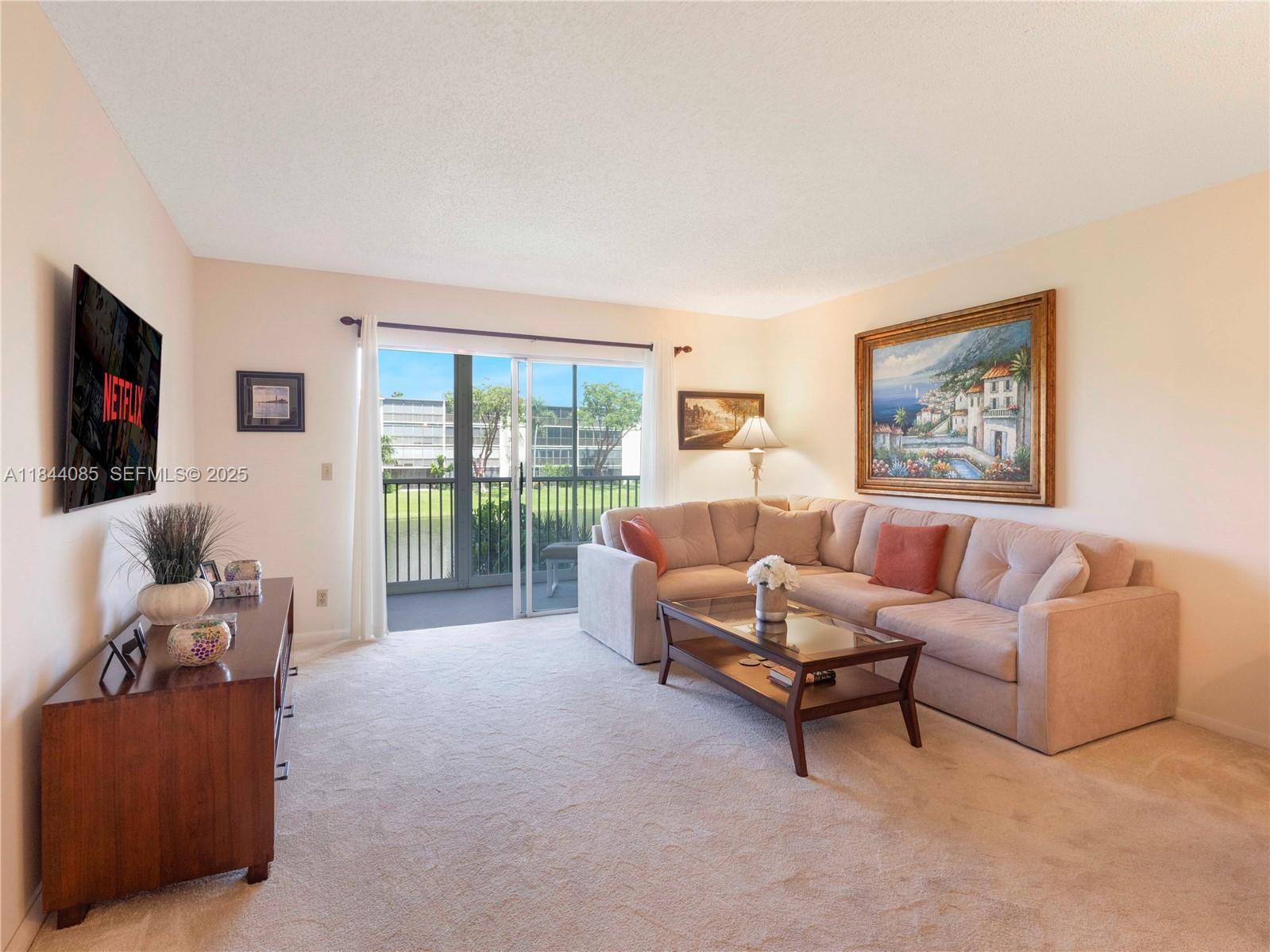 A living room features a beige sectional sofa, a coffee table, and a wall-mounted television — 14360 Strathmore Lane # 203, Delray Beach FL 33446, DELRAY BEACH, FL