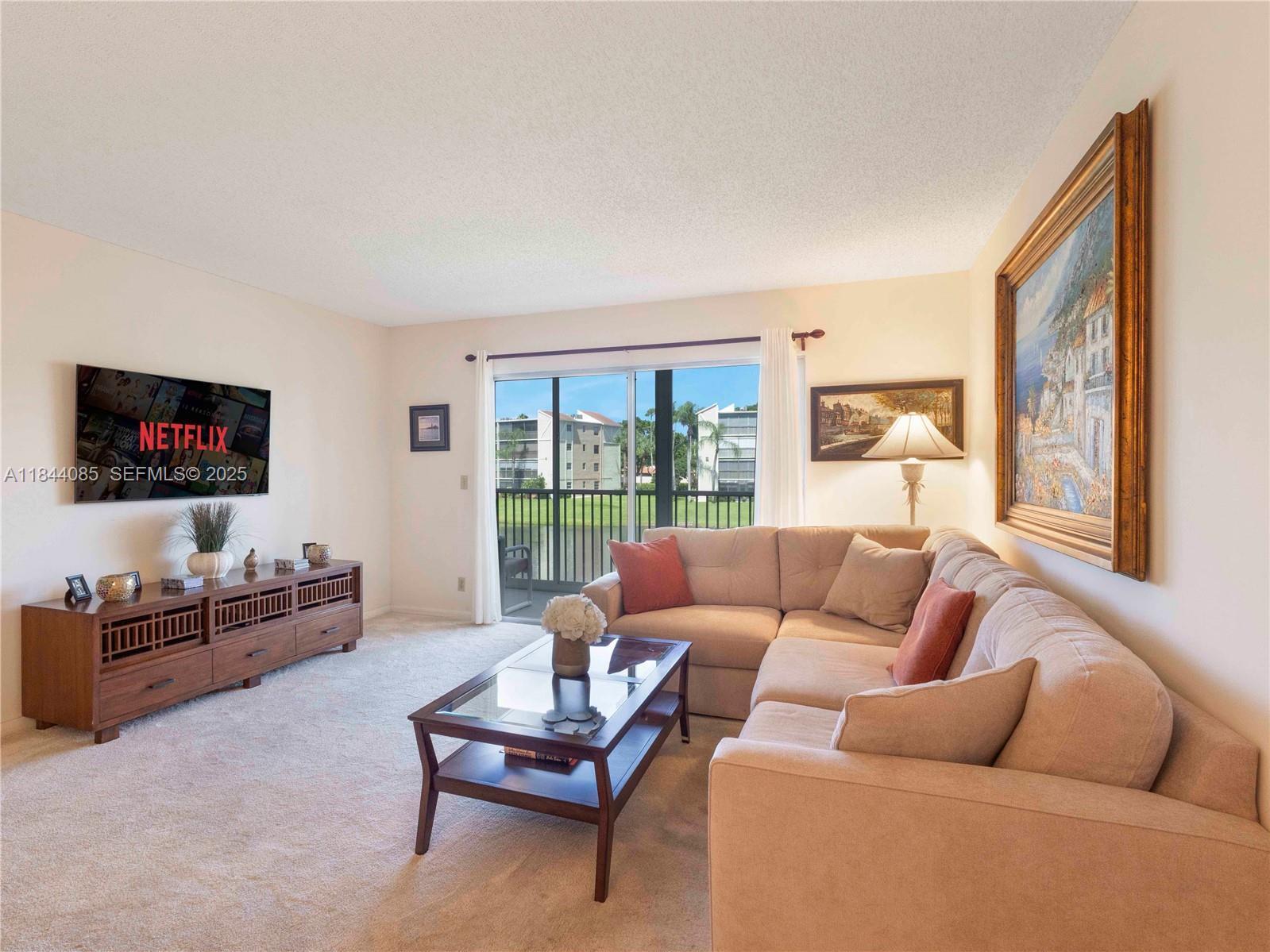 A living room features a beige sectional sofa, a glass coffee table, and a television — 14360 Strathmore Lane # 203, Delray Beach FL 33446, DELRAY BEACH, FL
