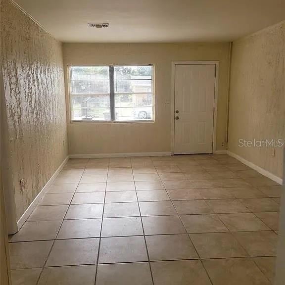 An empty room features beige tiled flooring, textured walls, a window with blinds, and a door — 508 BOOKER STREET, TITUSVILLE, FL