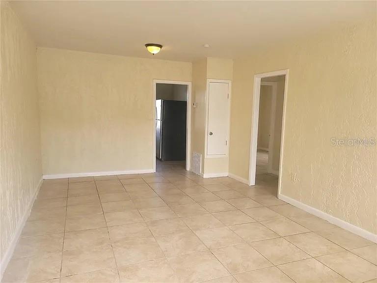 An empty room with beige tile flooring, textured walls, and two doorways leading to other rooms — 508 BOOKER STREET, TITUSVILLE, FL