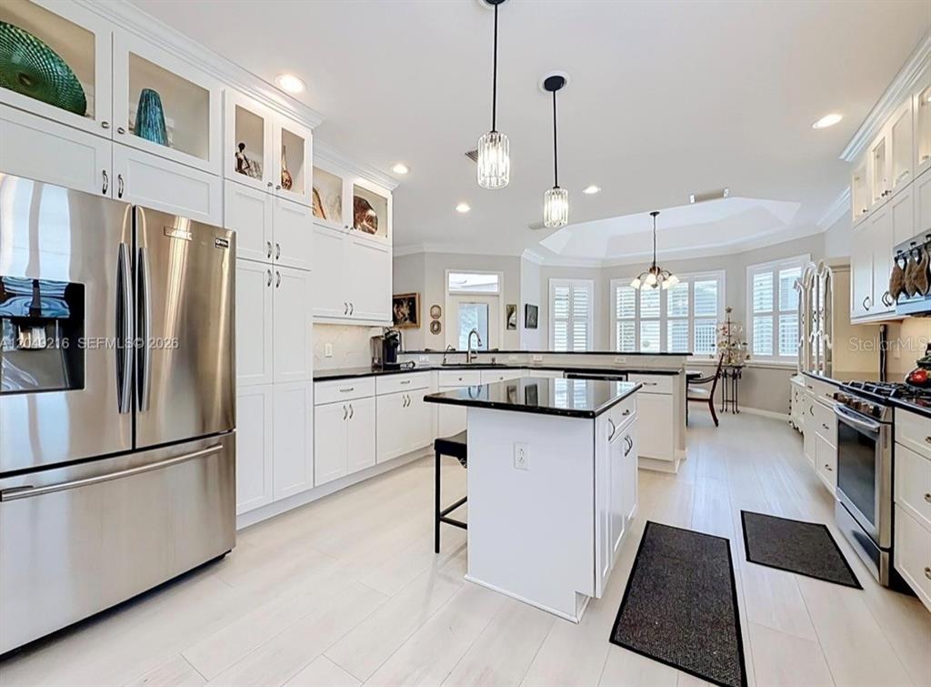 A bright kitchen features white cabinetry, stainless steel appliances, a black island, and light flooring — 1637 WESTMINSTER COURT, THE VILLAGES, FL