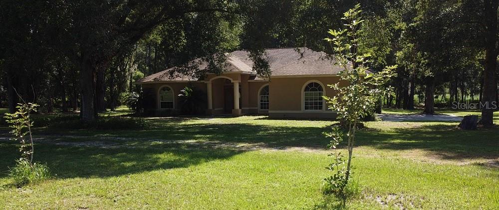 A tan, single-story house with an arched entryway sits on a grassy lot with trees — 2484 CULBREATH ROAD, BROOKSVILLE, FL