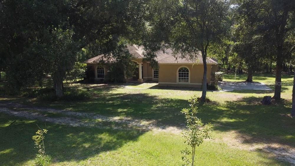A tan, single-story house with a shingled roof sits on a large, tree-filled lot — 2484 CULBREATH ROAD, BROOKSVILLE, FL