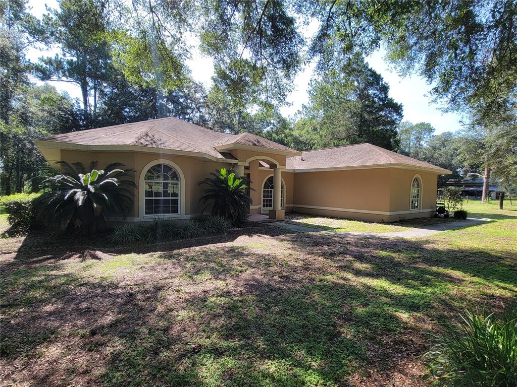 A tan, single-story house with a hip roof and arched windows sits on a wooded lot — 2484 CULBREATH ROAD, BROOKSVILLE, FL