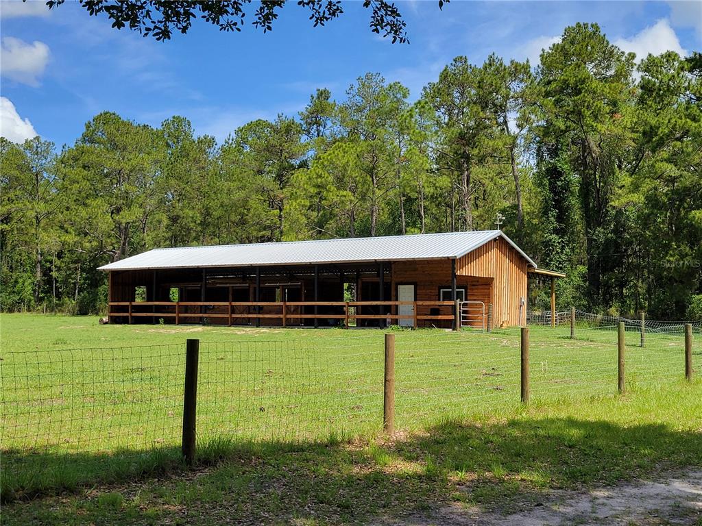 A wooden horse barn with a metal roof stands in a fenced grassy pasture — 2484 CULBREATH ROAD, BROOKSVILLE, FL