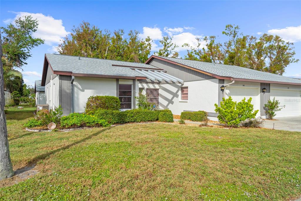 A single-story duplex with a gray shingled roof, stucco exterior, and a wooden pergola — 605 APPLE LANE, ENGLEWOOD, FL