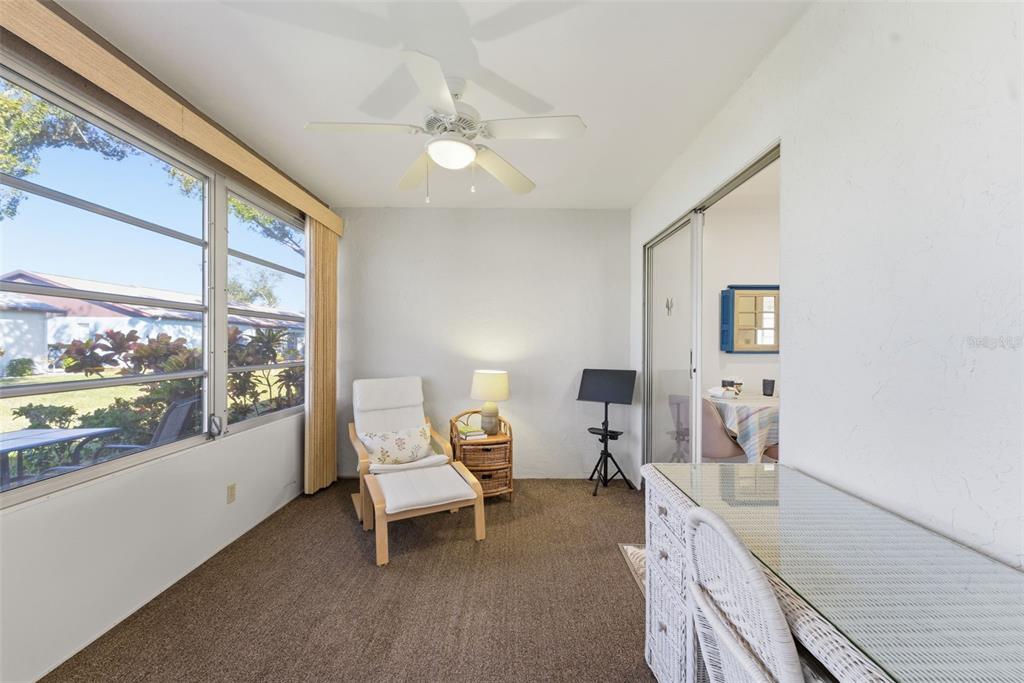 A sunroom features brown carpeting, a white armchair with an ottoman, and a glass-topped desk — 605 APPLE LANE, ENGLEWOOD, FL