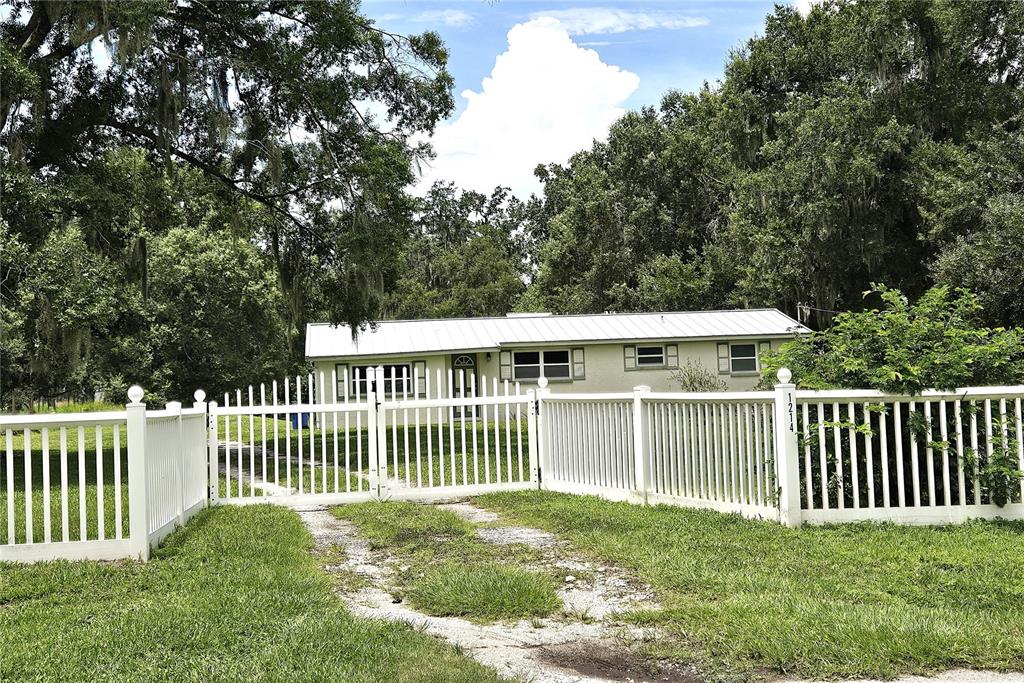 A single-story house with a white fence and a gated gravel driveway — 1214 JERRY SMITH ROAD, DOVER, FL