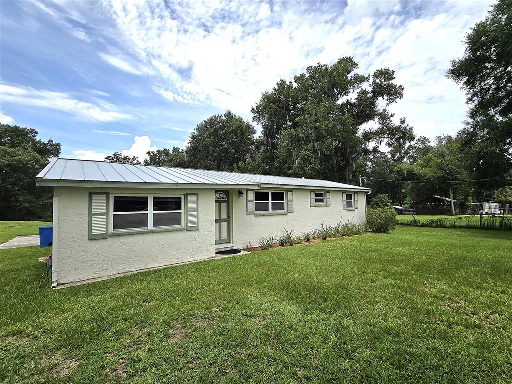 A single-story house with a metal roof and light-colored stucco siding sits on a lawn — 1214 JERRY SMITH ROAD, DOVER, FL