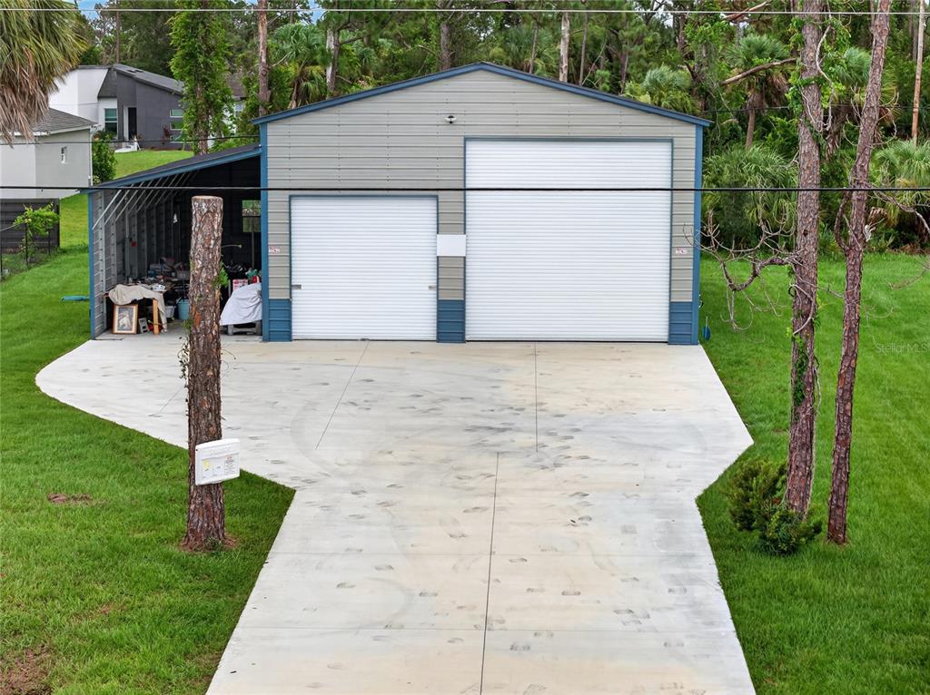 A detached metal garage with two roll-up doors and an open-sided carport on the left — 1264 S SALFORD BOULEVARD, NORTH PORT, FL