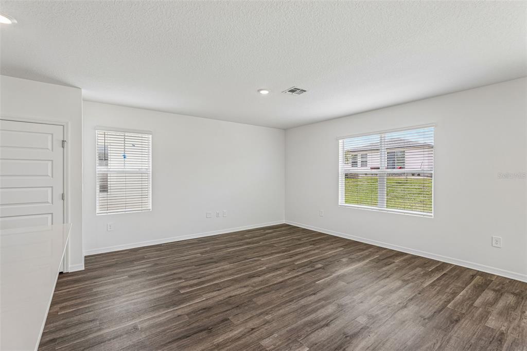 An empty room with white walls, wood-look flooring, two windows, and a white door — 4005 VALERIAN WAY, TAVARES, FL