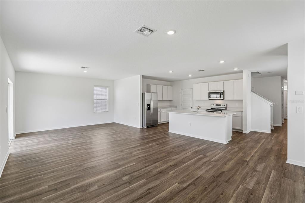An open-concept kitchen and living area features white cabinetry, a center island, and wood-look flooring — 4005 VALERIAN WAY, TAVARES, FL