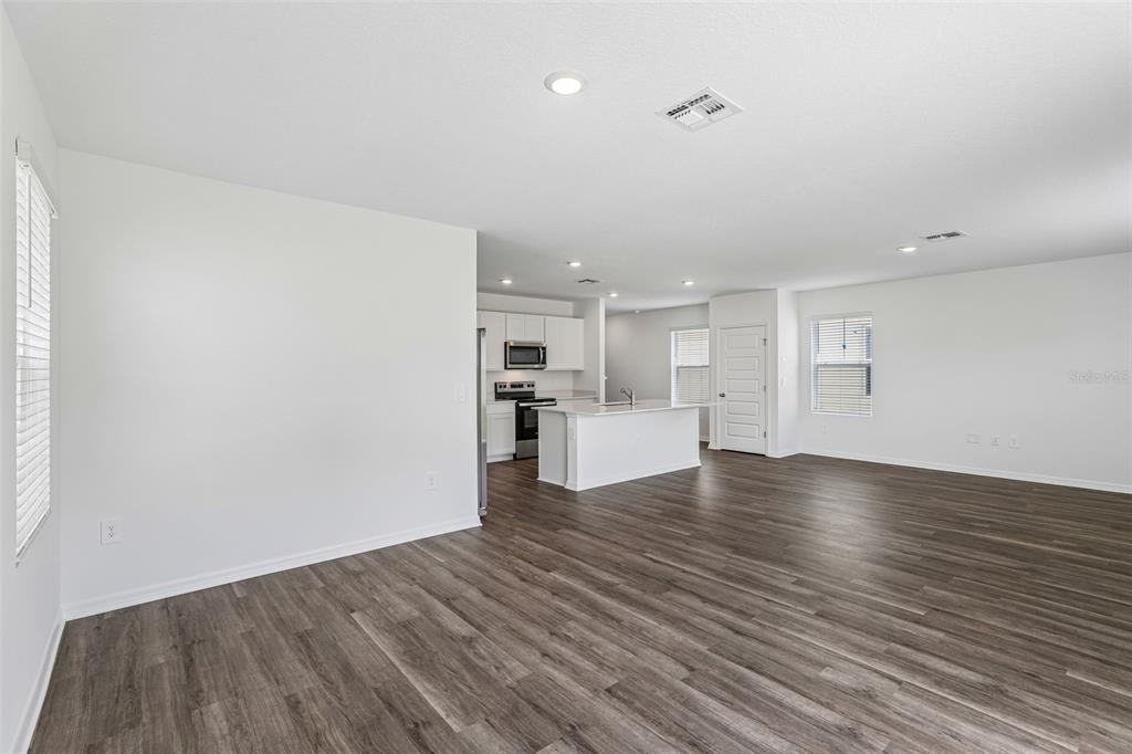 An open-concept living area features wood-look flooring, white walls, and a kitchen with white cabinets — 4005 VALERIAN WAY, TAVARES, FL