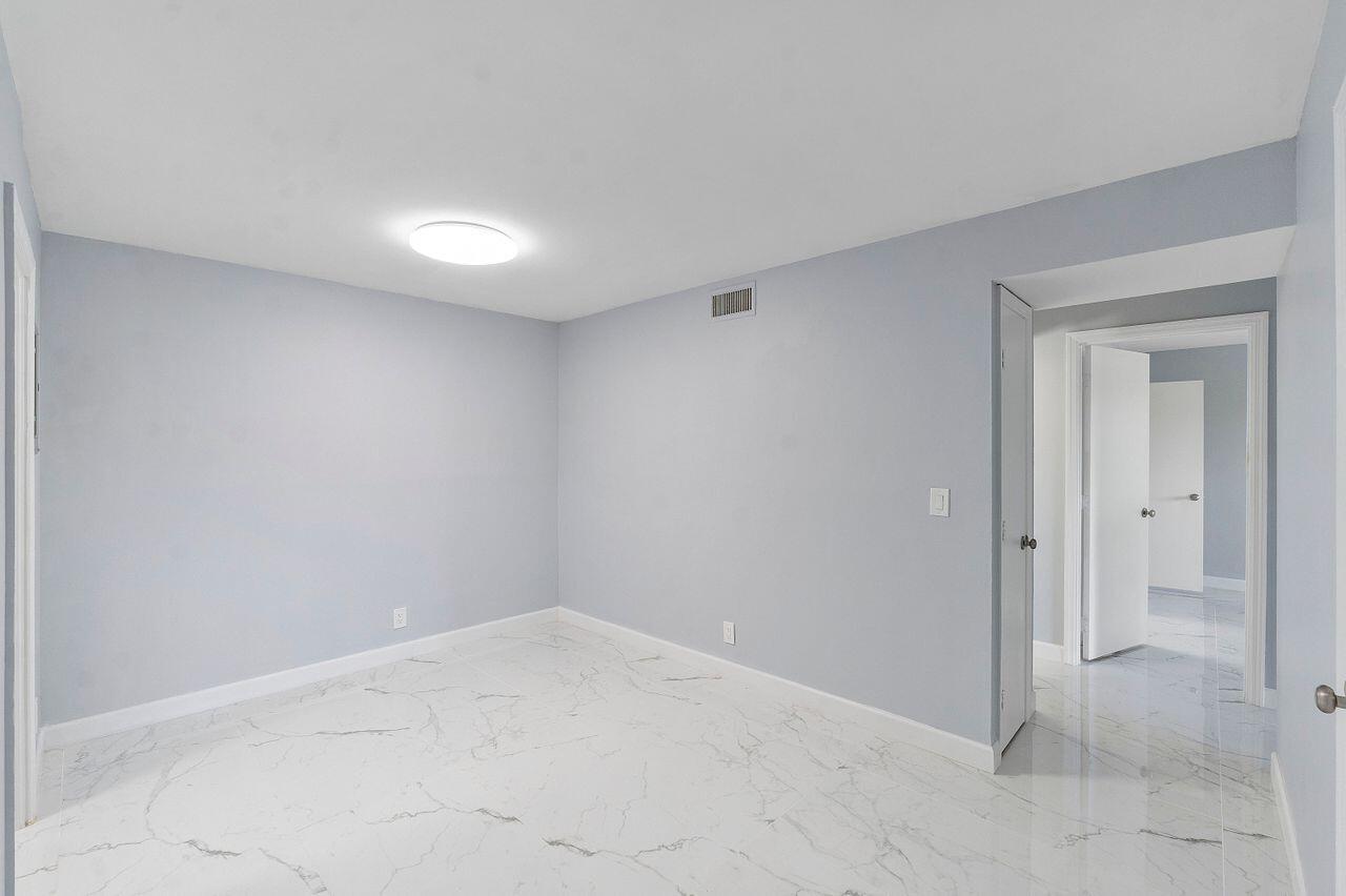 An empty room with light blue walls, white trim, and white marble-patterned tile flooring — 9960 Pineapple Tree Drive # 107, Boynton Beach FL 33436, BOYNTON BEACH, FL