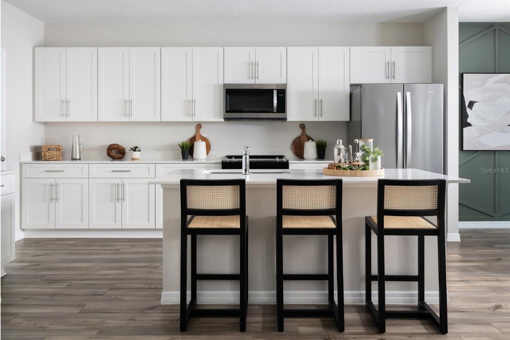 A modern kitchen features white cabinetry, stainless steel appliances, a central island, and three barstools — 36610 SAGEMOOR DRIVE, ZEPHYRHILLS, FL