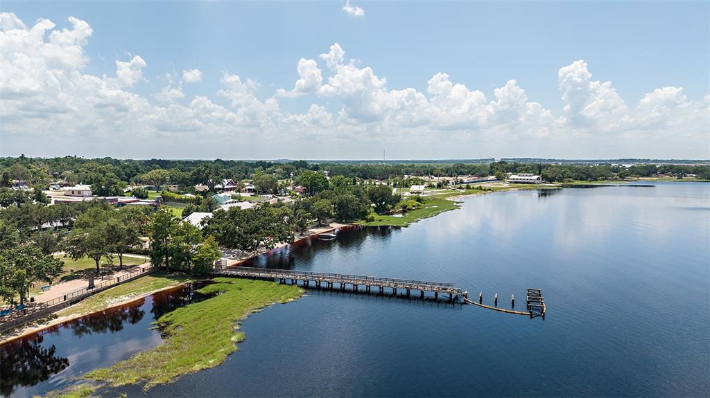 An aerial view shows a wooden pier extending into a lake near a grassy shoreline — 208 STREAMWATER WAY, GROVELAND, FL