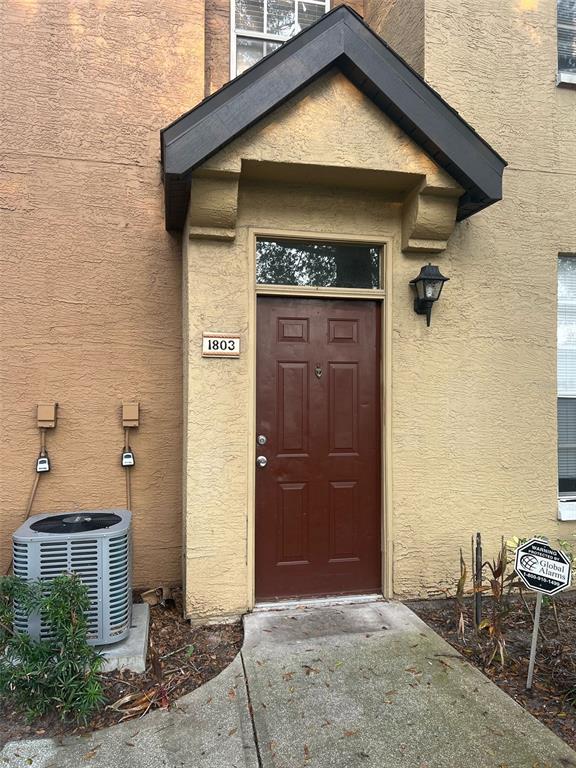 The exterior of a residential unit features a brown front door, a small porch, and an AC unit — 6368 RALEIGH STREET UNIT 1803, ORLANDO, FL