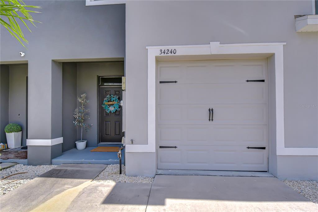 The exterior of a modern townhouse features a gray garage door and a recessed entryway — 34240 REDWOOD DAWN LANE, WESLEY CHAPEL, FL