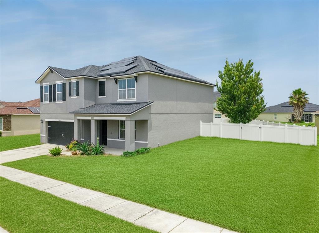 A two-story gray house with a dark roof, solar panels, and a white vinyl fence — 6115 GREY HERON DRIVE, WINTER HAVEN, FL